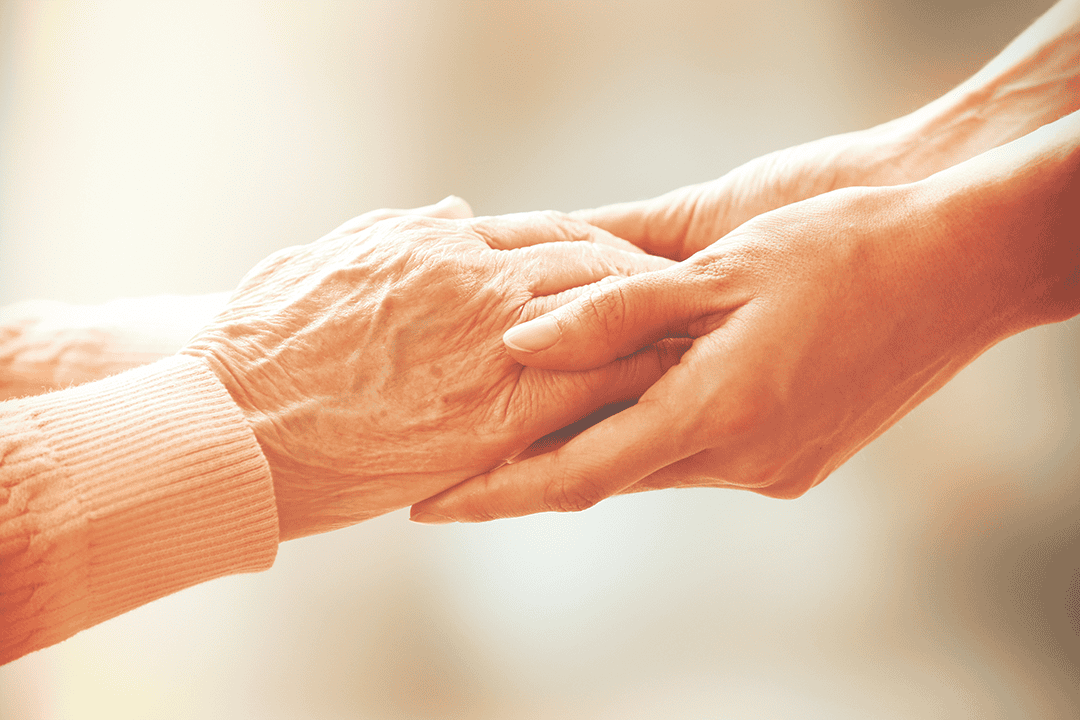 Carer holds client's hand in palliative care service